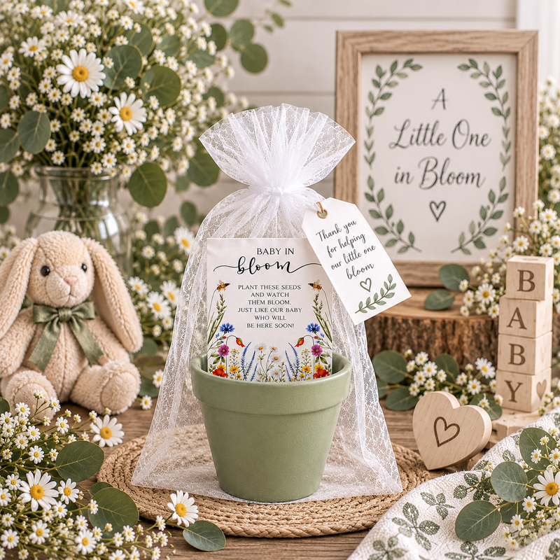 A soft green terracotta pot holding a Baby in Bloom wildflower seed packet, wrapped in white organza with a thank-you tag, styled with a plush bunny, BABY blocks, daisies and a framed A Little One in Bloom sign