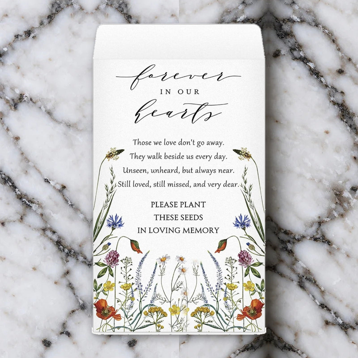 The Forever in Our Hearts memorial seed packet, printed with watercolour wildflowers and a remembrance verse, lying on white marble